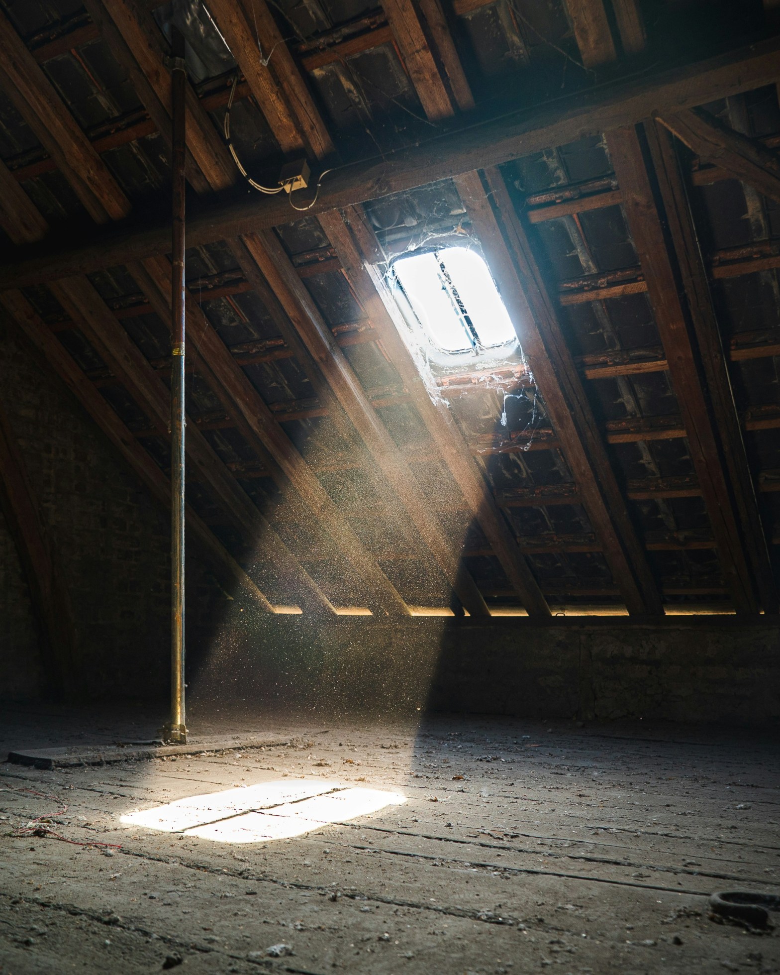 Dusty unfinished attic space with sunlight streaming through a single window