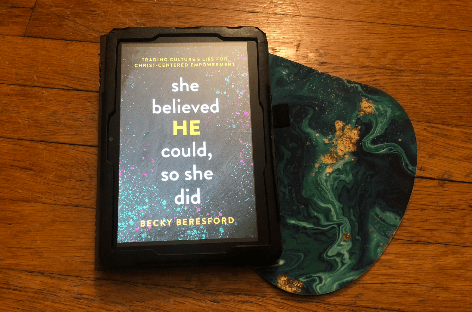 book "She Believed HE Could, So She Did" by Becky Beresford with a multicolored blob (teal/gold) off to one side and a wood background