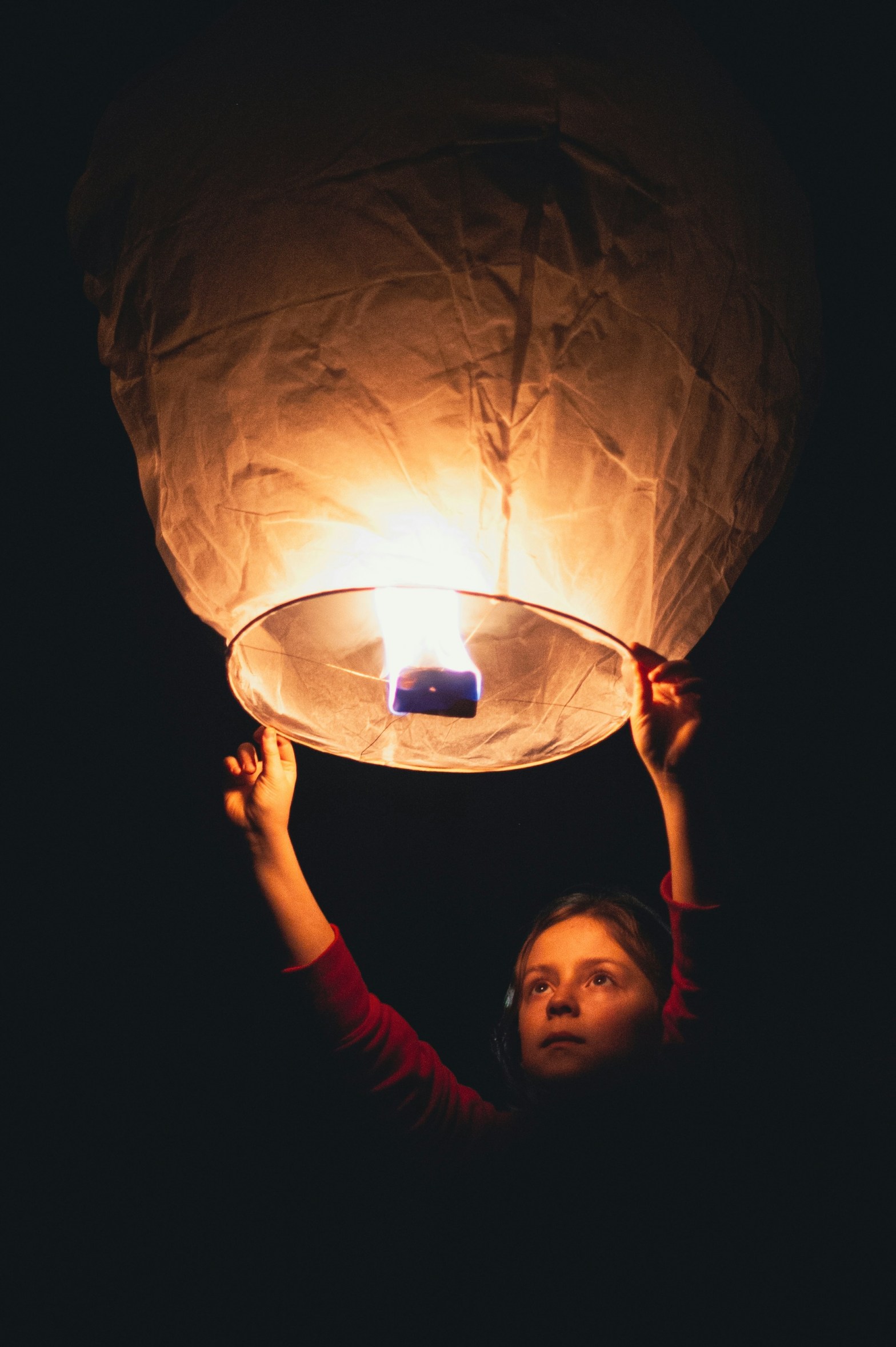 pitch black background with child holding and about to release a lit Chinese lantern